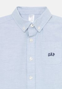 Camicia button-up azzurro chiaro con colletto, dotata di taschino sul petto e logo "GAP" ricamato in blu navy. Realizzata in un tessuto testurizzato.