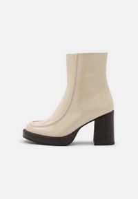 Stivale alla caviglia in pelle lucida beige con punta arrotondata, cuciture definite e tacco a blocco, dotato di una finitura in legno scuro.