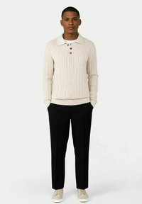 Kremfarget ribbestrikket genser med krage og tre knapper, kombinert med slim-fit svart bukser og lyse sneakers.