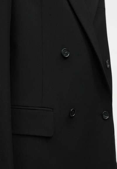 Μαύρο διπλόκουμπο σακάκι με λεία υφή, στενή γραμμή, δύο κουμπιά και πλαϊνή τσέπη με διακριτική υφή.