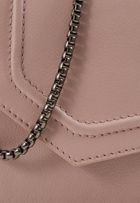 Primo piano di una borsa in pelle rosa pallido con cuciture dettagliate e una catena metallica argentata chunky.