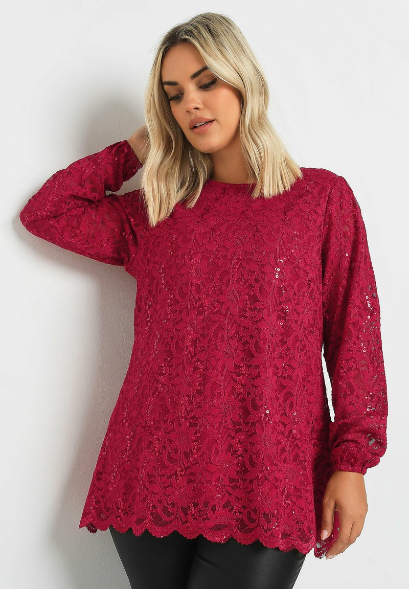 Top in pizzo rubino con maniche lunghe, orlo ondulato e paillettes. Presenta un collo rotondo e motivi floreali intricati su un tessuto testurizzato.