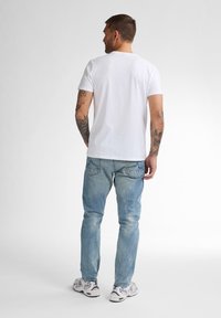 Camiseta blanca de algodón y pantalones vaqueros de denim azul claro, con un corte relajado, costuras visibles y un ligero desgastado en la tela.
