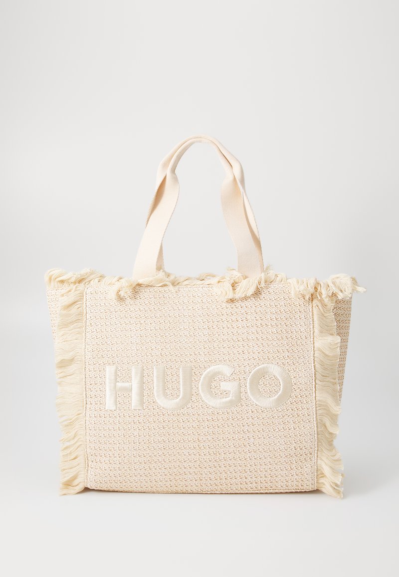Cream woven tote bag with frayed edges and embossed "HUGO" logo in the center. Features sturdy fabric handles for easy carrying.