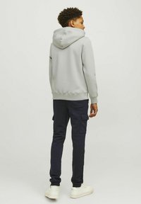 Lichtgrijze hoodie met een buidelzak, gecombineerd met marineblauwe cargobroek met zijzakken en witte sneakers. Bijpassende texturen en kleuren.