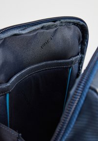 Interno di una borsa blu navy con una texture liscia, caratterizzato da scomparti e dettagli azzurri. Cuciture decorative lungo i bordi.