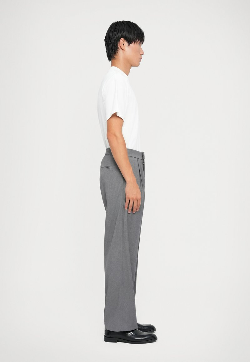 Pantalons gris ajustés avec un design à jambe droite, associés à un t-shirt blanc uni à manches courtes. Des chaussures en cuir noires viennent compléter le look.