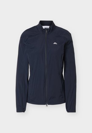 Lekka granatowa kurtka z pełnym zamkiem z przodu, stójką, długimi rękawami i małym białym logo na lewej piersi.