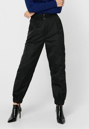 Osoba nosząca czarne spodnie cargo ze ściągaczami, czarny pasek, niebiesko-czarną, paskowaną bluzkę z długim rękawem oraz czarne botki na obcasie.