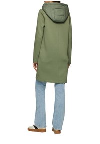 Olivgrüner langer Hoodie mit einer ge quilteten Kapuze, geradem Schnitt, weichem Stoff, langen Ärmeln und Seitennähten, kombiniert mit hellblauen Jeans.