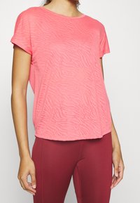 T-shirt z krótkim rękawem w jaskrawym różowym kolorze z teksturowanym wzorem w paski zebry. Lekki, luźny krój z okrągłym dekoltem.