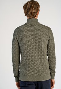 Zielony sweter dzianinowy z teksturowanym wzorem w diamenty, wysokim kołnierzem oraz ściągaczami przy rękawach i u dołu. Widok z tyłu ukazuje skomplikowany design.
