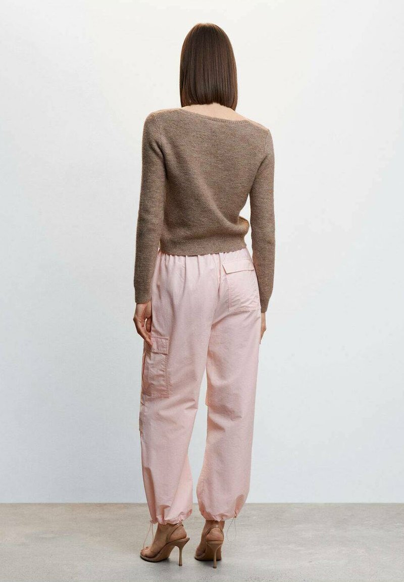 Suéter de punto marrón, ajustado en la cintura; pantalones cargo rosas con bolsillos laterales y tobillos entallados; modelo con tacones beige, visto desde atrás.