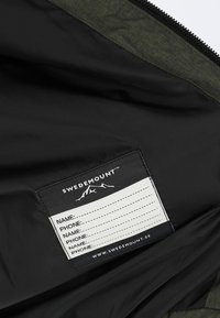 Giacca da esterno verde con fodera nera. Presenta un'etichetta con nome e righe vuote per le informazioni personali, logo in cima.