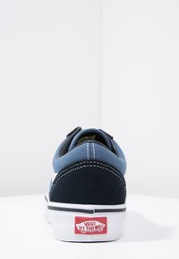 Baskets en toile bleu et marine avec une semelle blanche, des coutures contrastantes et un logo rouge "VANS OFF THE WALL" sur le talon.