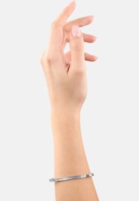 Bracciale in argento con superficie liscia e lucidata. Presenta una sottile linea di piccoli cristalli su un lato, indossato a mano.