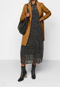 Brown wool blend coat over a black dress with gold heart patterns, paired with black ankle boots featuring a block heel. Black shoulder bag.
