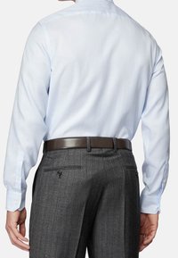 Uomo che indossa una camicia da dress a righe blu chiaro infilata in pantaloni da dress grigio scuro a righe, con una cintura in pelle marrone, mostrato da dietro.