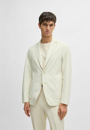Lys kremfarget dressjakke med en strukturert design, spiss krage og to frontlommer. Stoffet har en glatt tekstur og en lett glans.