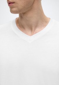 Λευκό t-shirt με λαιμόκοψη σε σχήμα V και απαλό ύφασμα, με διακριτική ραφή κατά μήκος της γραμμής του λαιμού και απλό, καθαρό σχέδιο.