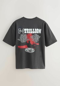 T-shirt noir avec texte blanc "F-1 TRILLION", une silhouette rouge d'une personne, des titres de chansons et le logo "POSTY CO." au dos.