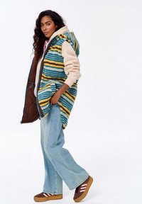 Mitmevärviline vest siniste, kollaste ja pruunide triipudega; tekstuuriga materjal; kapuuts; ees taskud; koos beeži kapuutsiga ning lõdva teksapaariga.