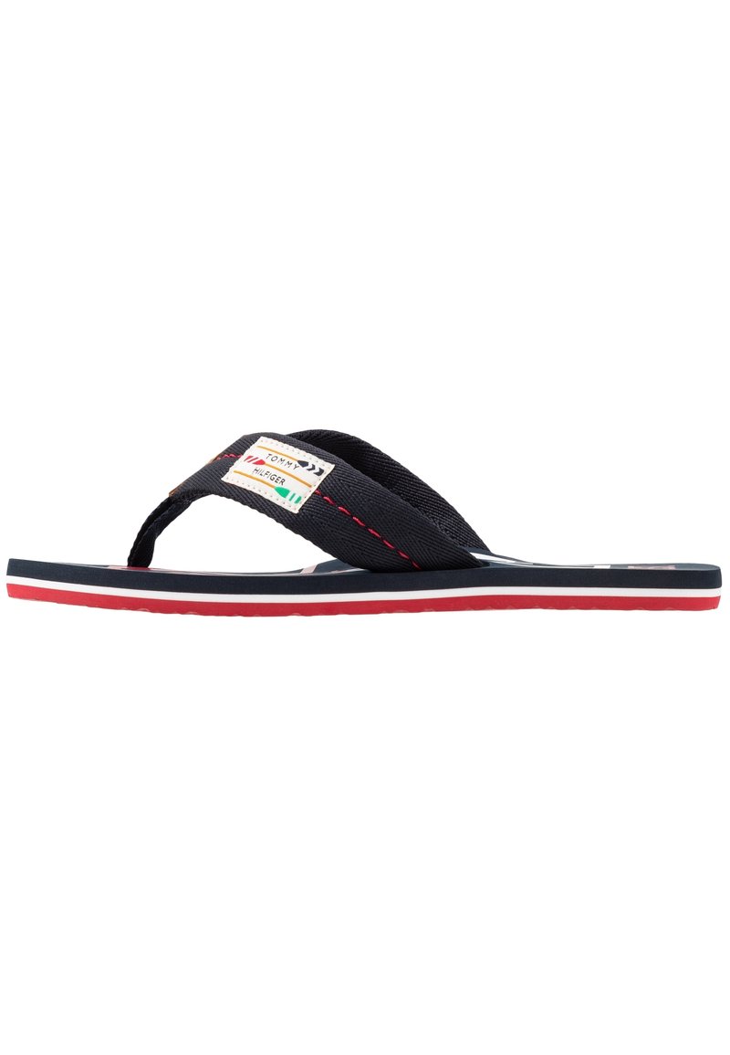 Marineblaue Flip-Flops mit Stoffriemen, rotem und weißem Mittelsohlenbereich, mit einem Markenlabel am Riemen. Strukturierte Sohle für besseren Halt.