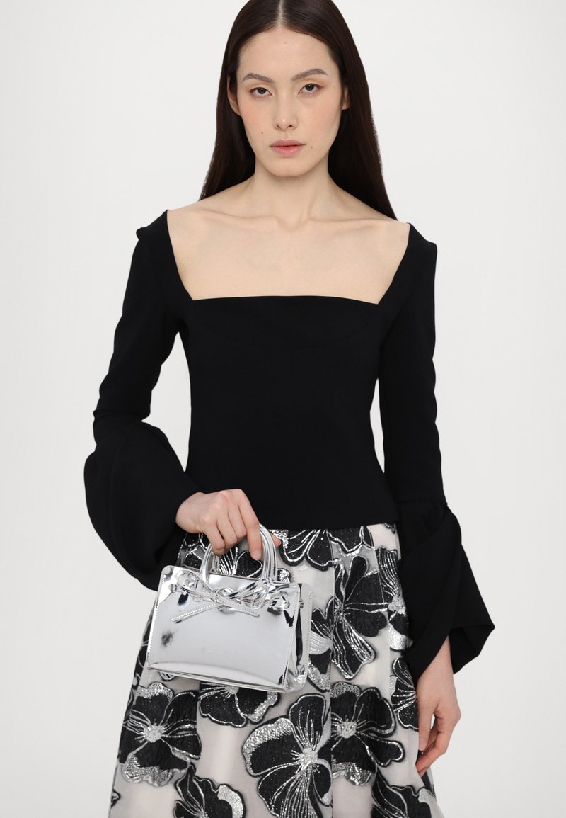 Maglietta nera a maniche lunghe con scollatura quadrata, abbinata a una gonna con motivo floreale e una piccola borsa argento con dettaglio a fiocco.