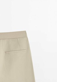 Jupe beige à coupe droite, avec une ceinture plate et une unique poche passepoilée horizontale au dos sur fond blanc.