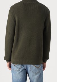 Pull en maille vert foncé avec une finition texturée, doté d'un col montant et de manches longues, associé à un jean en denim bleu clair.