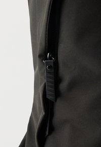 Μαύρο υφασμάτινο σακίδιο πλάτης με μαύρο φερμουάρ με υφή και λεία επιφάνεια. Ο σχεδιασμός είναι μίνιμαλ, χωρίς εμφανή λογότυπα ή μοτίβα.