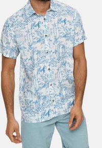 Korte mouwen shirt van lichtblauwe stof met een boom- en bergpatroon, voorzien van bruine knopen en een relaxed fit.