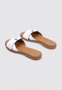 Chanclas blancas con correas texturizadas cruzadas, plantilla marrón claro y suelas marrones claras con costuras blancas contrastantes.