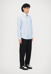 Světle modrá pruhovaná košile s dlouhými rukávy a límečkem na knoflíky, doplněná černými volnými kalhotami a černými mokasínami s bílými detaily.