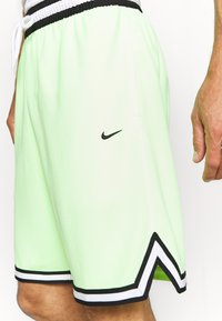 Pantalones cortos atléticos verde claro con un logo negro de Nike, cinturilla negra y un ribete en blanco y negro que contrasta en el dobladillo y los lados.