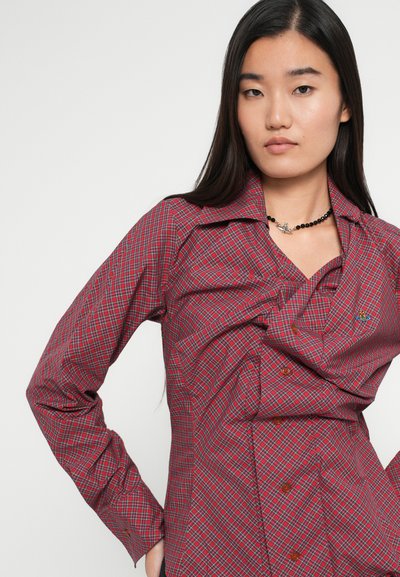 Camisa em xadrez vermelho e marinho com mangas longas, frente com botões e um detalhe de design envolvente. Apresenta um pequeno logótipo no peito.