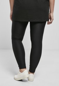 Collants noirs à côtes avec une coupe ajustée, associés à des baskets blanches. Les collants ont une texture lisse et se resserrent aux chevilles.