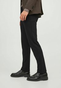 Černé kalhoty na míru s úzkým střihem, vyrobené z hladké látky. V kombinaci s lesklými černými mokasíny a hnědým kostkovaným blejzrem.