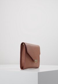 Růžově zbarvená kabelka z umělé kůže se zapínáním na klopu, zlatými kovovými doplňky a texturovaným povrchem. Obdélníkový tvar pro kompaktní uskladnění.