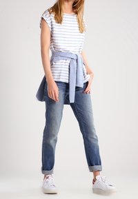 T-shirt a righe blu e bianche con maniche arrotolate, legato con un tessuto azzurro chiaro. Abbinato a jeans in denim con risvolto e sneakers bianche.