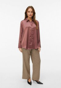 Satin mauve knapup skjorte med lange ærmer, parret med beige brede bukser og spidse sorte hæle. Glat tekstur og klassisk krave.