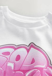 T-shirt in cotone bianco con una grande stampa in stile graffiti rosa, caratterizzata da lettere arrotondate e un sottile effetto ombra attorno al testo.