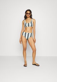 Conjunto de bikini em duas peças com um padrão em zigzag azul claro e preto. O top tem um decote redondo e a parte de baixo de cintura alta oferece cobertura.