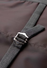 Sangle en tissu gris avec boucle métallique argentée reposant sur un fond en tissu marron foncé et lisse.