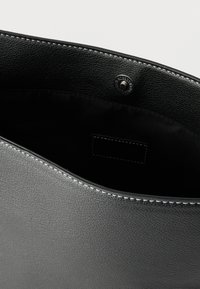 Μαύρη δερμάτινη τσάντα με υφή εξωτερικά και λεία εσωτερική επιφάνεια, εξοπλισμένη με μαγνητικό κούμπωμα και εμφανή ραφές στα άκρα.