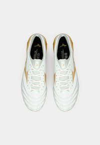 Λευκά αθλητικά παπούτσια με χρυσές λεπτομέρειες, υφασμένο δέρμα στο πάνω μέρος, παραδοσιακό κλείσιμο με κορδόνια και μαλακό μαξιλαράκι στο πέλμα. Σχεδιασμός με επίπεδη σόλα για σταθερότητα.