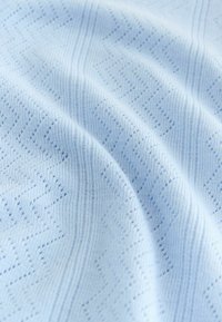 Tissu bleu clair avec un motif en zigzag texturé et un tricot fin côtelé, présenté en plis doux.