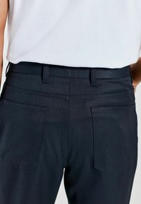 Black denim pants with a fitted design, featuring two back pockets and belt loops, displayed from the rear against a neutral background.
