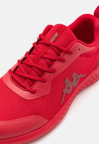 Red athletic shoe with a mesh upper, textured fabric, matching laces, and smooth rubber accents. Features a logo in contrasting material.