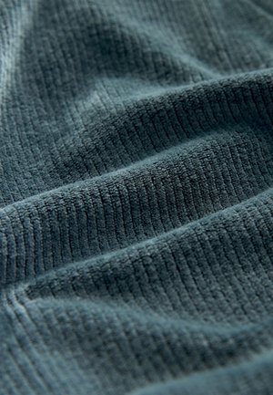 Sötét türkiz színű, texturált szövet, keskeny, függőleges bordázattal. Puha, plüss felület finom fényes árnyalattal. Ideális bútorkárpitokhoz vagy textíliákhoz.